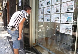 Un joven mira pisos en venta en el escaparate de una agencia inmobiliaria.