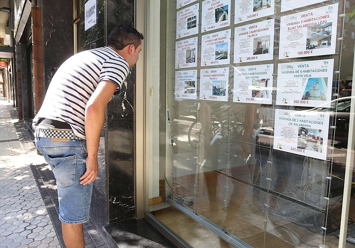 Un joven mira pisos en venta en el escaparate de una agencia inmobiliaria.