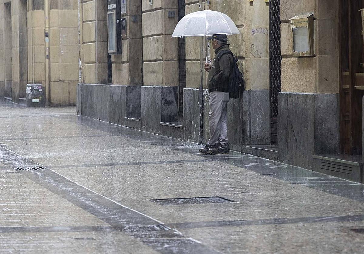 Un hombre se refugia de la lluvia en la Parte Vieja de Donostia.