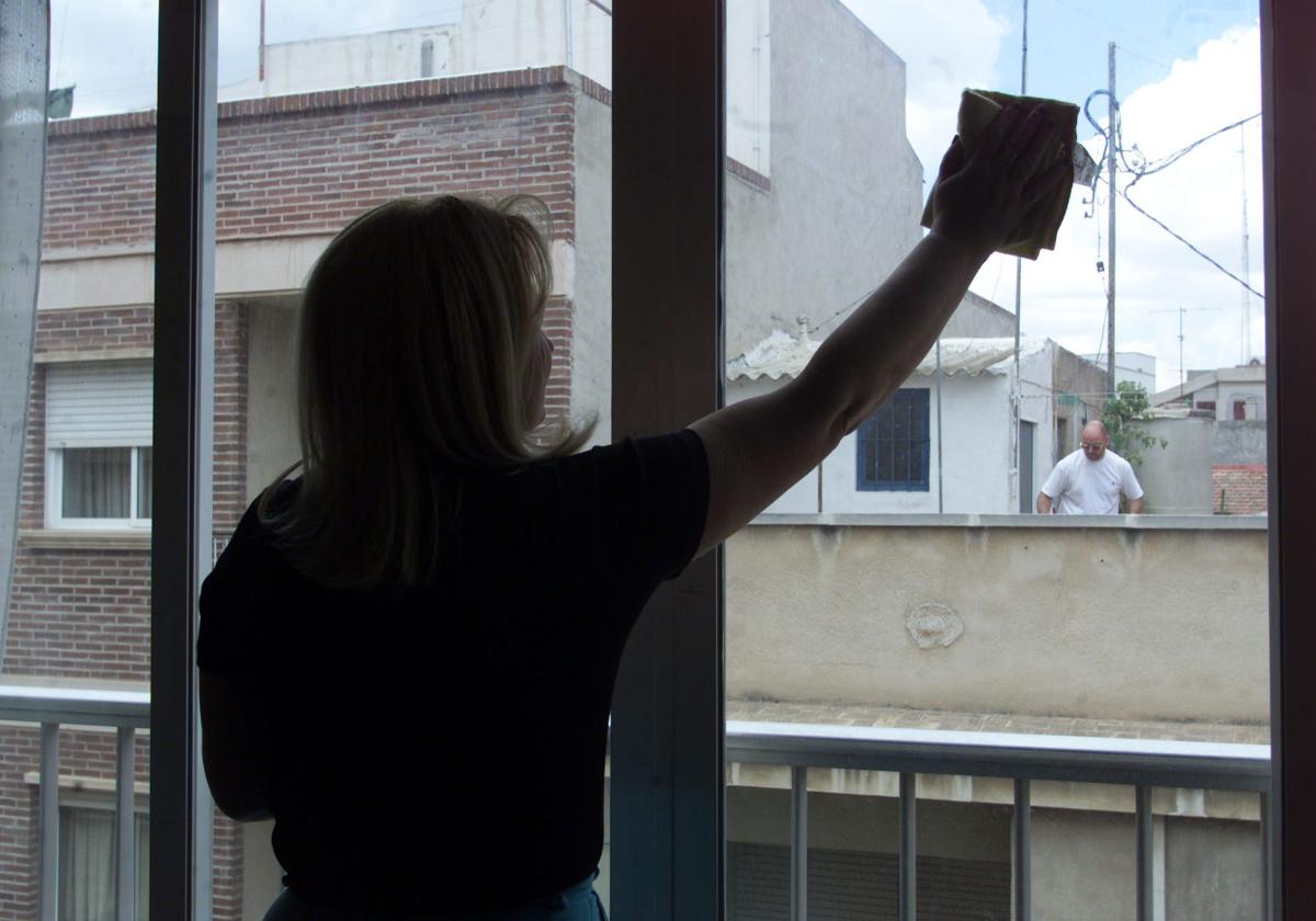 Una empleada de hogar limpia los cristales de la ventana de una vivienda.