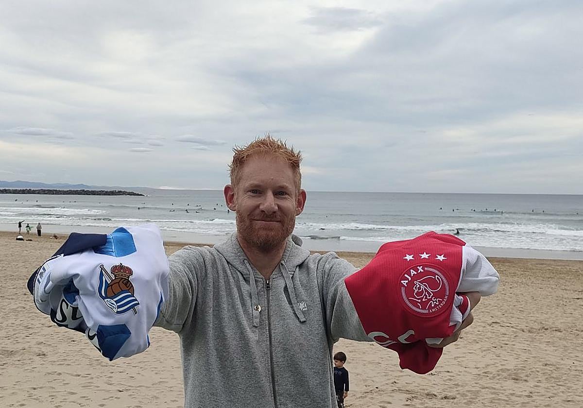 Ben Parham, un aficionado de la Real Sociedad y el Ajax, posa con las camisetas de los respectivos equipos en La Zurriola.