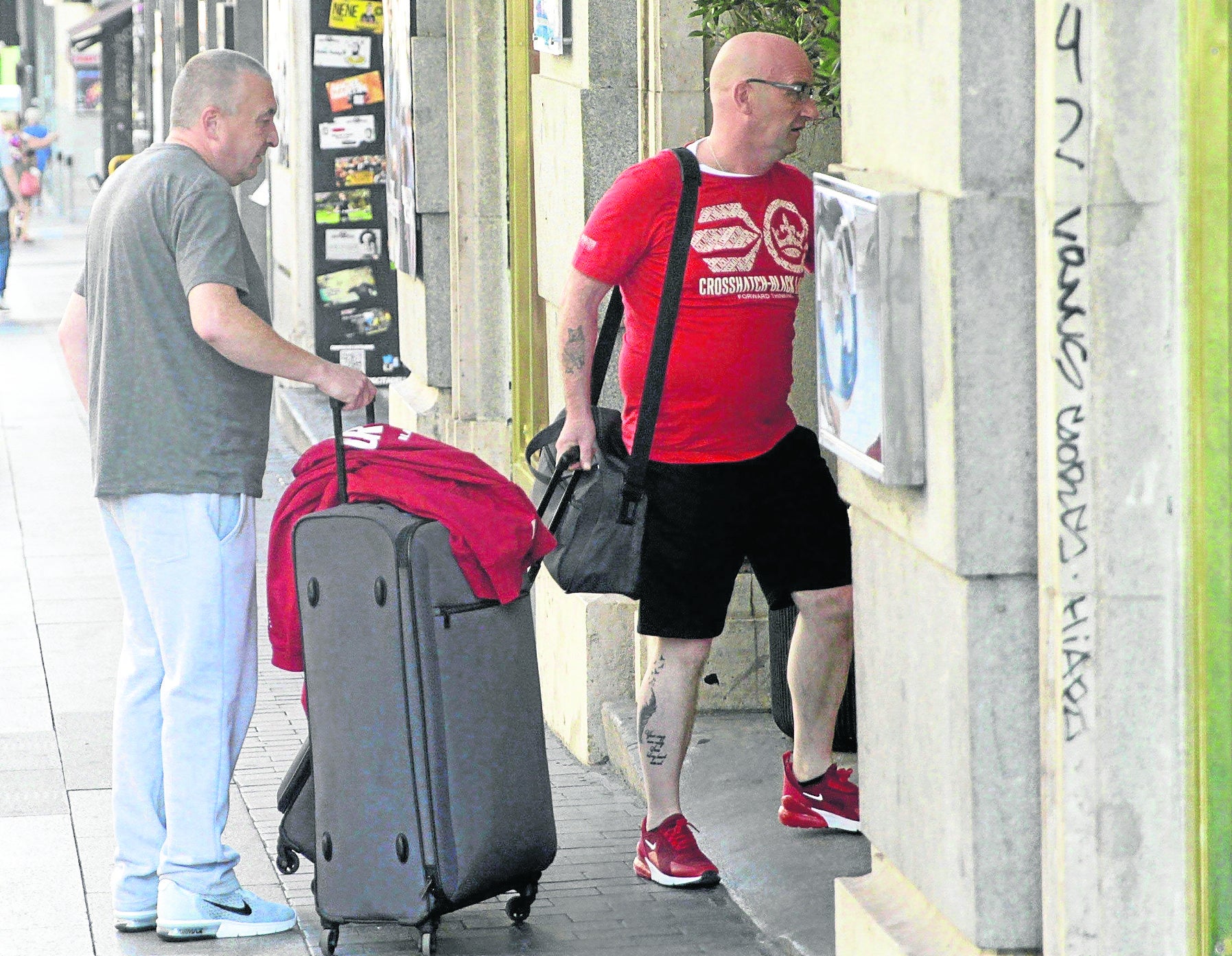 Dos personas acceden al interior de un portal con sus maletas.