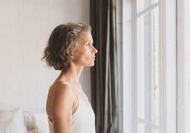 Una mujer mira a través de la ventana de un dormitorio.