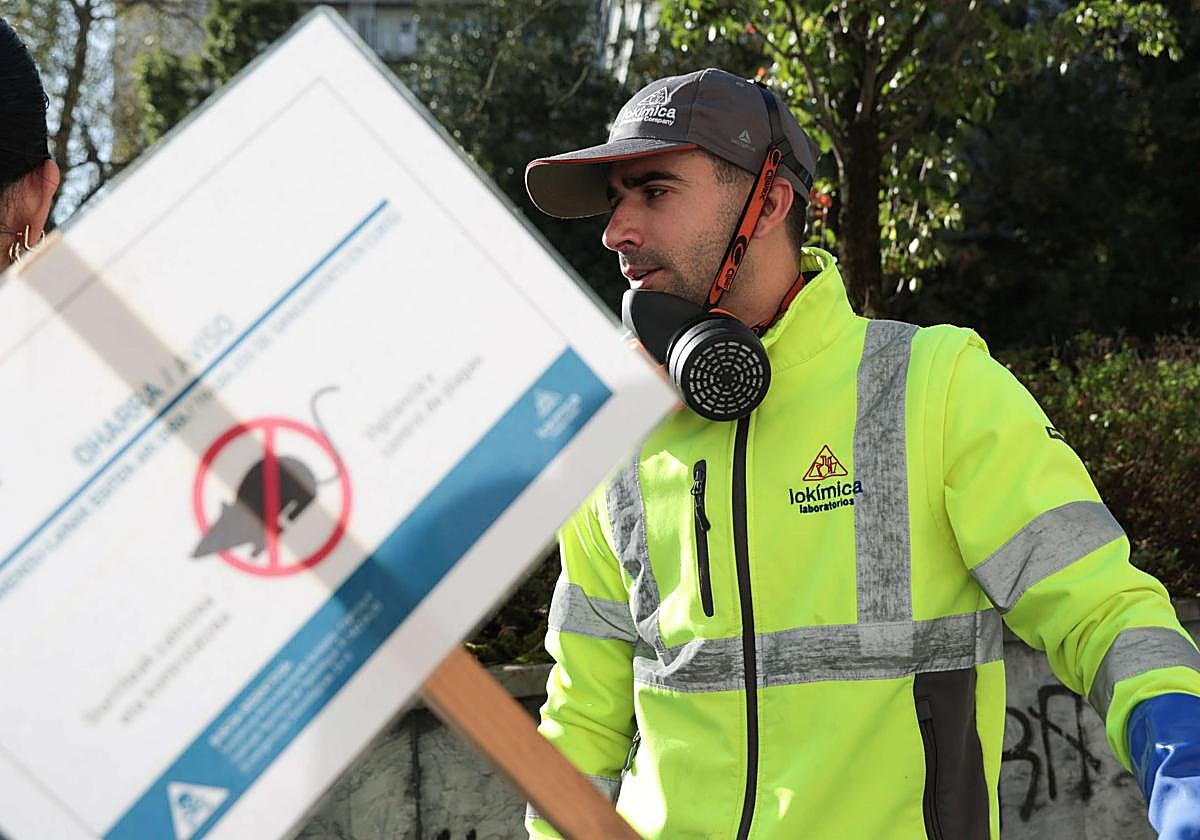 Un operario del ayuntamiento coloca una señal avisando de la presencia de veneno para ratas en una zona verde.