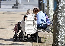 Una mujer en silla de ruedas, junto a su cuidadora.