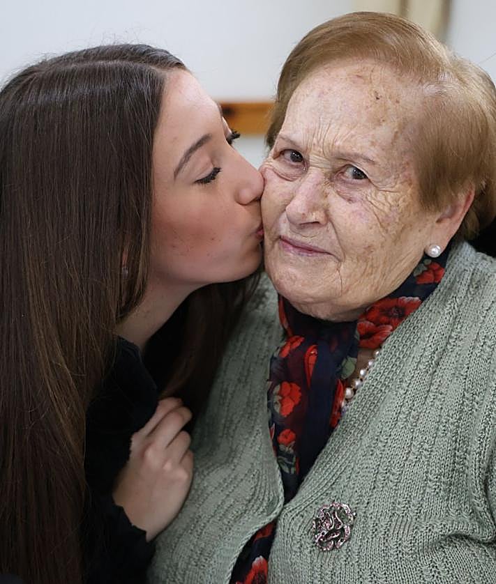 Imagen secundaria 2 - Ona Pérez, de 16 años, le pinta las uñas de color rosa a Josefina Cano; Conchi enseña la manicura y las uñas que una de las alumnas le pintó en color rojo; y Naia le da un cariñoso beso a Basil.