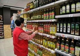 Una trabajadora de Eroski coloca diferentes botellas de aceite de oliva en un supermercado.