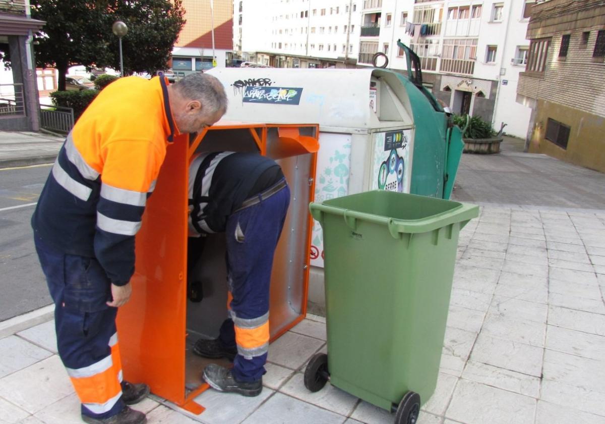 Operarios instalan el contenedor en la plaza Foruen. Al lado, el recipiente al que caen los botes.