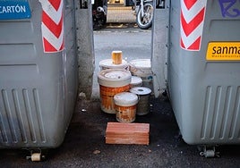 Botes de pintura depositados de manera ilegal entre dos contenedores.