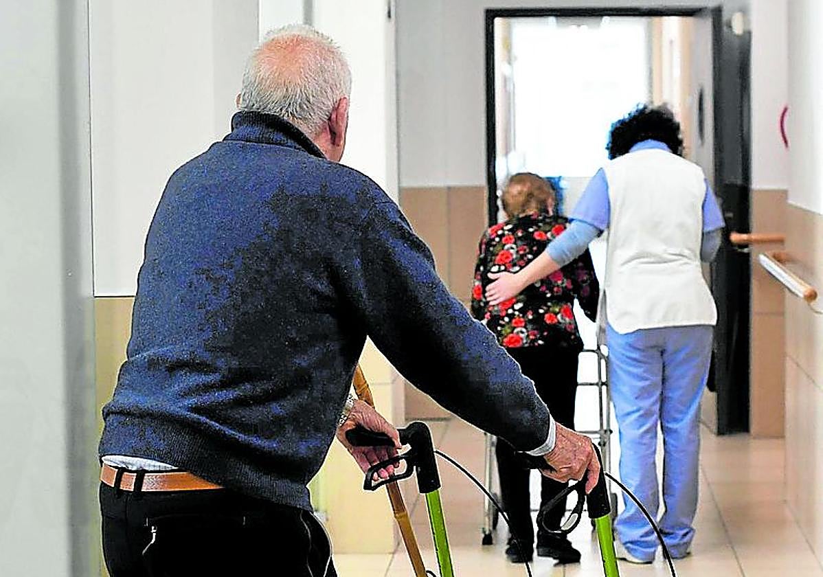 Un hombre camina con ayuda por el pasillo de una residencia.