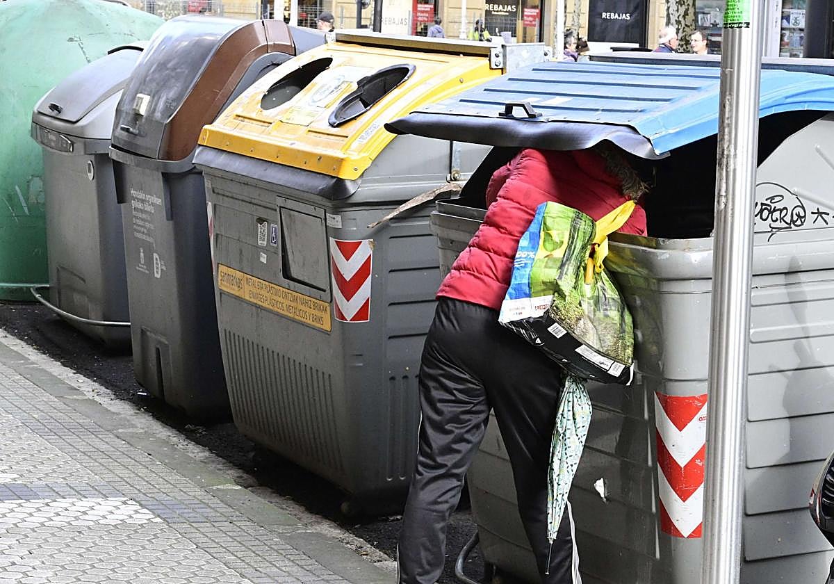 Una persona en situación de calle rebusca entre un contenedor de basura en Donostia.