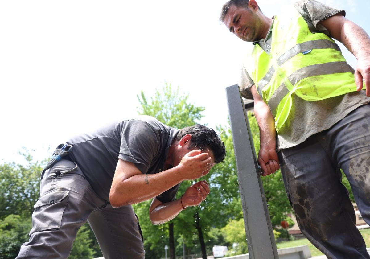 Técnicos de telecomunicaciones se refrescan con el agua de una fuente.