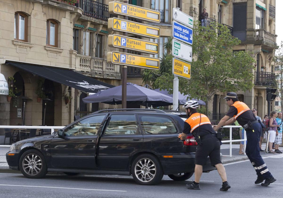 Dos agentes de Movilidad empujan un turismo averiado en la plaza Euskadi de Gros.