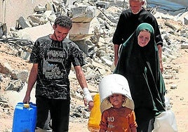 Un grupo de palestinos regresa con varios galones de agua potable de un punto de distribución, en una ciudad de Gaza asolada por la guerra.
