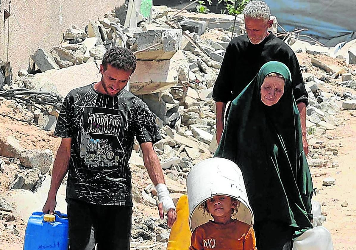 Un grupo de palestinos regresa con varios galones de agua potable de un punto de distribución, en una ciudad de Gaza asolada por la guerra.