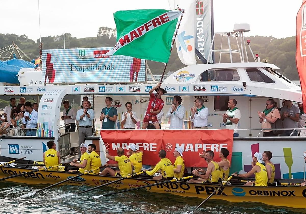 Gorka Aranberri ondeando la bandera tras la regata de Hondarribia, con los remeros alegres por el triunfo.
