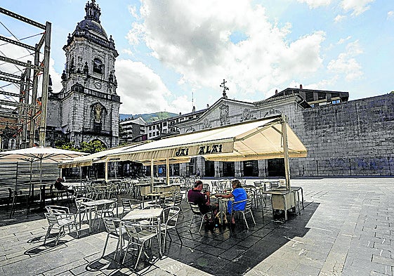 Una pareja se refugia del sol en una terraza con toldo en una desierta plaza de Elgoibar.