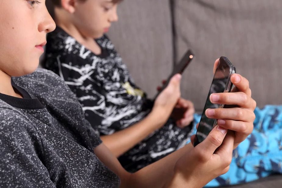 Dos niños miran sus teléfonos móviles; la mayoría de ellos se hace un con un 'smartphone' a los 12 años.
