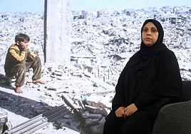 Nahla, que porta un hiyab negro, posa ante una imagen de su Gaza natal en ruinas.