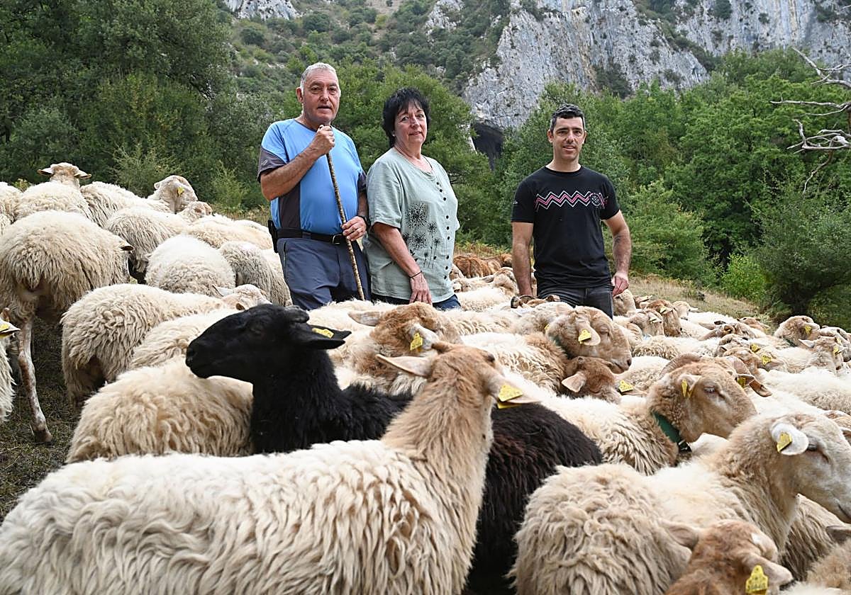 Jose Mari, Eli y Arkaitz posan junto a sus ovejas con la cueva que da nombre a su queso a fondo.