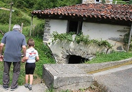 Un hombre contempla con su nieto el canal de agua, junto al histórico molino de Lastur.