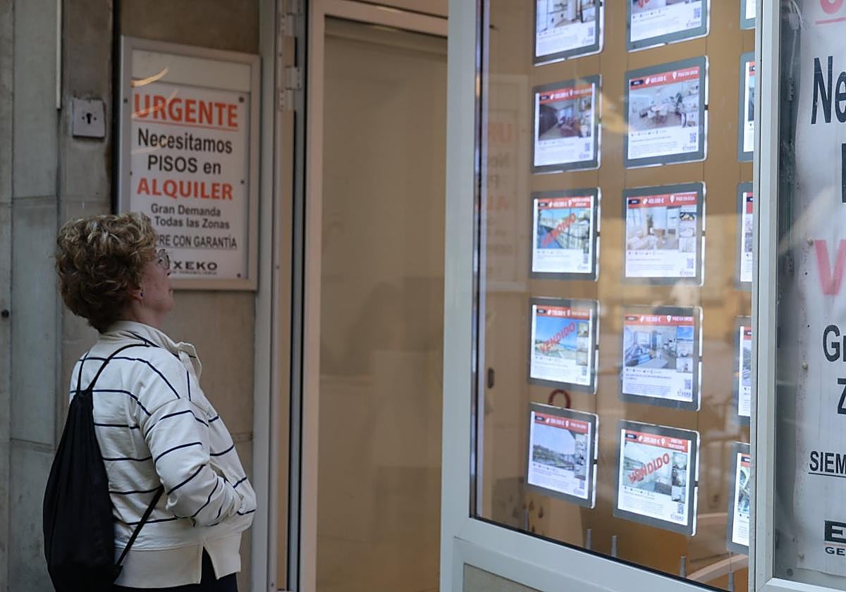 Una mujer observa el escaparate de una inmobiliaria de Gros con un cartel que dice 'Urgente, necesitamos pisos en alquiler, gran demanda'.