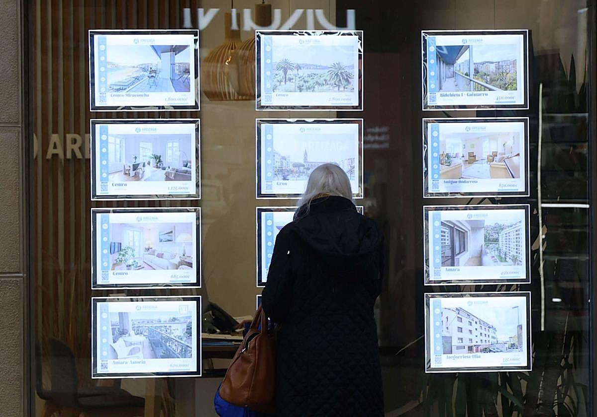 Una mujer observa la oferta inmobiliaria en el escaparate de una agencia.