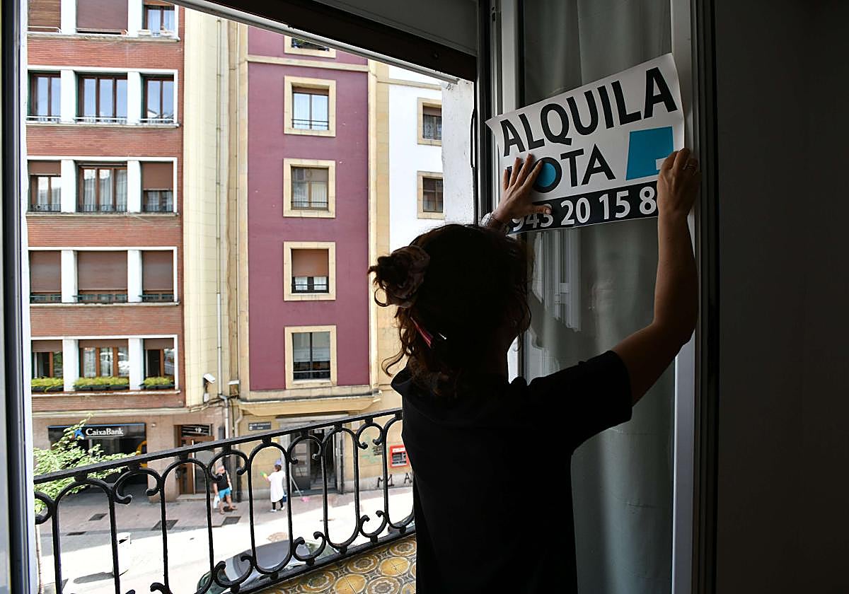 Una agente inmobiliaria coloca un cartel de 'se alquila' en un piso de Eibar.