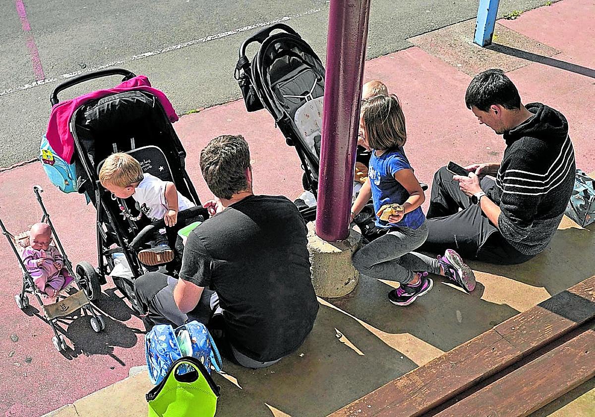 Dos padres dan de merendar a sus hijos en una zona de juegos.