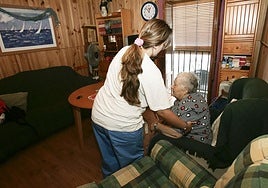 Una mujer es ayudada a levantarse del sillón por su cuidadora.