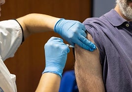 Una sanitaria inocula una vacuna a un hombre.