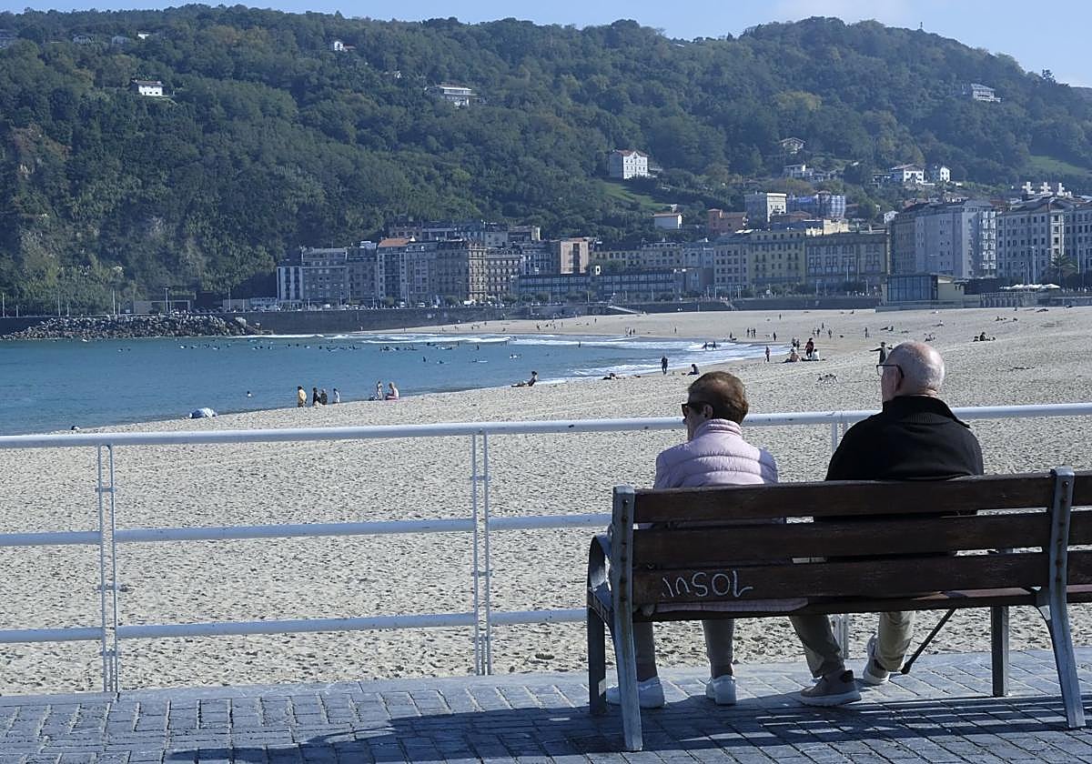 Dos personas observan desde un banco el aspecto de la playa de la Zurriola, con cielos despejados.