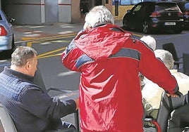 Una persona cuida a un mayor en silla de ruedas.