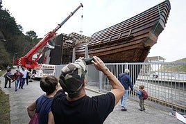 Un paseante plasma en su móvil cómo la grúa deposita las piedras que servirán de lastre al galeón.