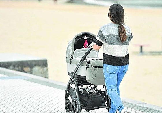 Una madre pasea a su bebé en un carrito junto a la playa de Ondarreta.