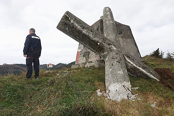 Un agente de la Ertzaintza junto a la derribada cruz, ayer por la mañana en la cumbre de Morkaiku.