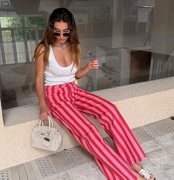 Mujer con camiseta blanca básica de tirantes y pantalón de rayas rosa y rojo.