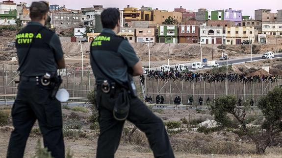 Miembros de la Guardia Civil vigilan a inmigrantes subsaharianos encaramados a la valla de Melilla. 