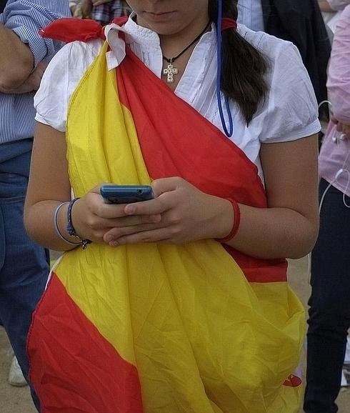 Una joven envuelta en la bandera de España revisa su smartphone. 