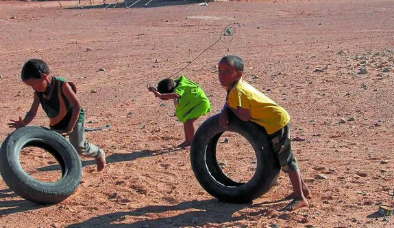 Varios niños juegan en el desierto descalzos con unos viejos neumáticos.
