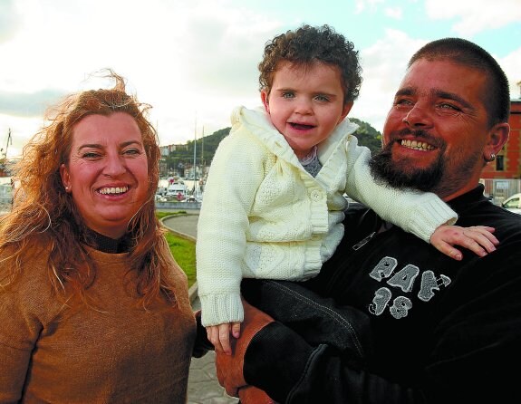 La pequeña Eunate, sonriente en los brazos de su aita, David, y su ama, Irene.