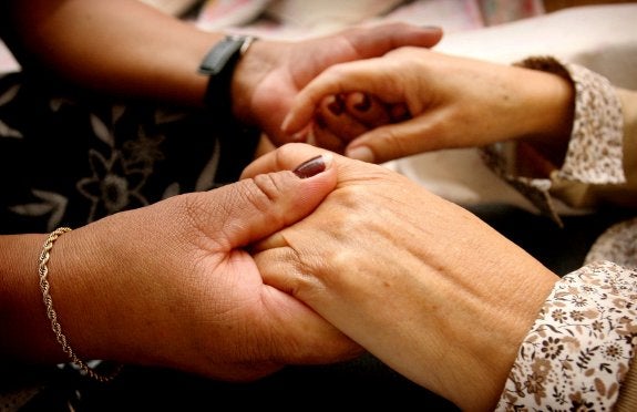 Una mujer sostiene las manos de la anciana a la que cuida.