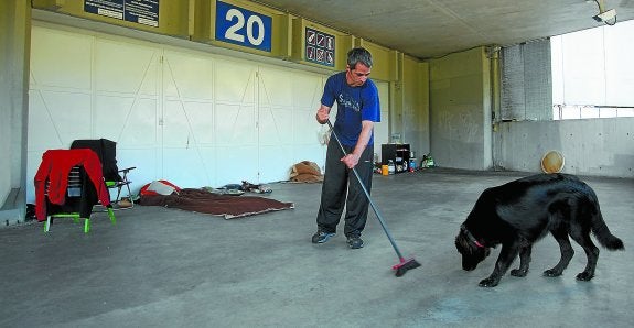 Rubén trata de tener limpio el soportal del estadio en el que vive. A la izquierda, ordena los víveres junto al hornillo en el que cocina y con Mundo, un perrazo del que no se separa.
