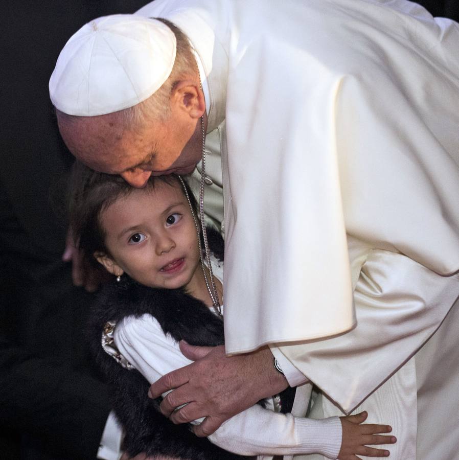 El papa Francisco besa a una niña en la cabeza.