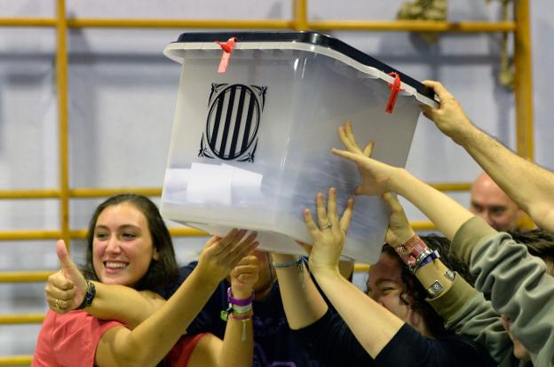 Varios jóvenes sostienen una de las urnas con centenares de votos en su interior al cierre de la jornada electoral en Cataluña. Una joven llora ante varios agentes antidisturbios. 