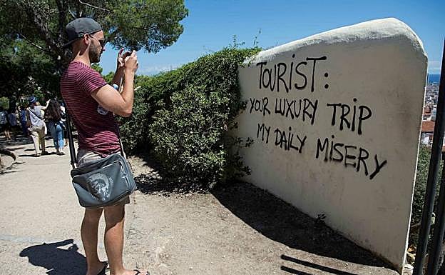 Un turista junto a una pintada en una pared que dice 'Turista: tu viaje de lujo mi miseria diaria'. 