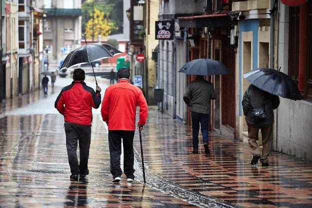 Dos hombres se cobijan con un paraguas en la calle Rivero. 