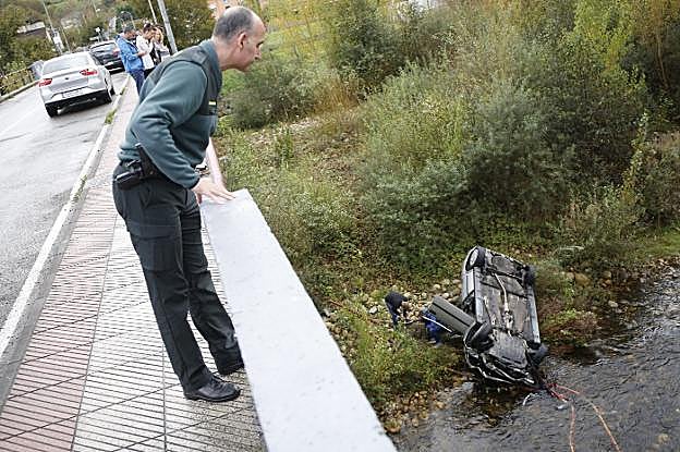 Un guardia civil observa desde el puente el coche que se precipitó hasta el río mientras los ocupantes salen del vehículo. 