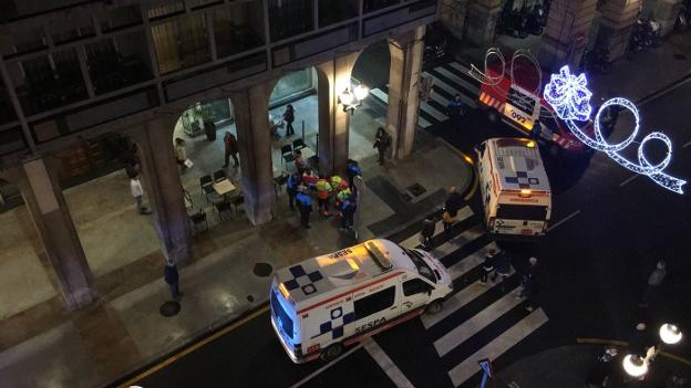 Los sanitarios atienden al motorista, sentado en un banco. 