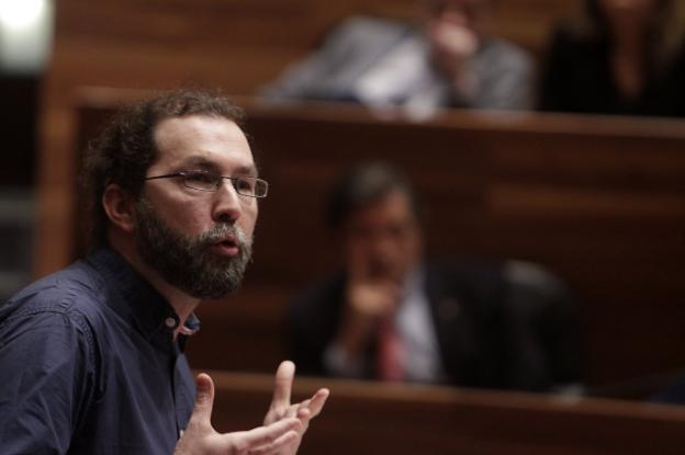 El portavoz de Podemos, Emilio León, interviene en el pleno, con Javier Fernández al fondo, sentado en su escaño. 